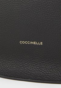 Black textured leather wallet featuring a gold embossed logo "COCCINELLE" near the bottom. Smooth edges with subtle stitching details.