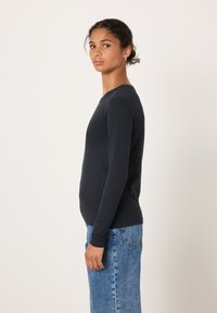 Mustast puuvillast pluus pikkade varrukatega, ümar kaelus, keha järgiv lõige ja sile tekstuur, kombineeritud kõrge vöökohaga siniste teksapükstega.