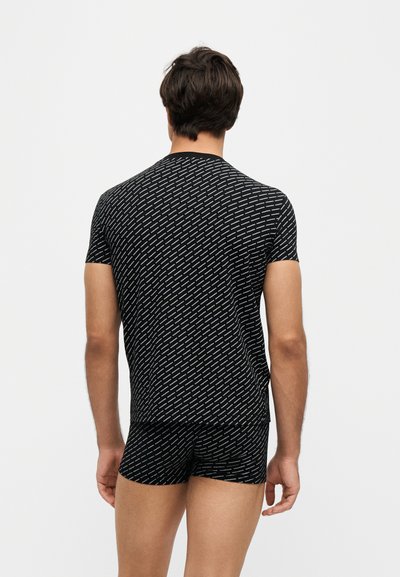 Homme vu de dos portant une chemise noire à manches courtes et un short assorti avec un petit motif de texte diagonal blanc.