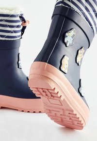Stivali da pioggia impermeabili navy con suola rosa, caratterizzati da tessuto a strisce bianche nella parte superiore e toppe in gomma a tema animale colorate sui lati.