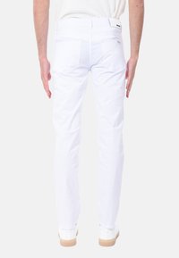 Pantaloni in denim bianco con design affusolato, dotati di due tasche posteriori e passanti per la cintura, abbinati a sneakers bianche e a una maglietta chiara.