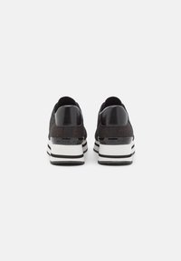 Černé sportovní boty s texturovaným textilním svrškem, lesklým pata kapsou a bílou podrážkou s černými a šedými pruhy.