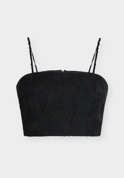 Crop top noir avec fines bretelles ajustables et texture jacquard florale sur un fond clair uni.