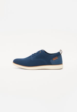 Navy blue lace-up shoes made from mesh material with a textured surface, contrasting white sole, and a brown accent on the heel.