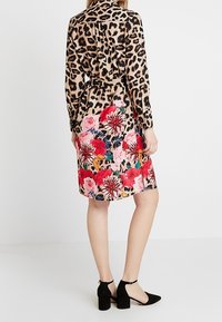 Chemise à manches longues à imprimé léopard avec taille ceinturée ; robe à motif floral avec des fleurs roses et rouges ; associée à des escarpins noirs à bride cheville.