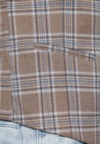 Koszula w kratę z brązowym, beżowym i niebieskim wzorem. Wykonana z teksturowanej tkaniny, z kieszonką na piersi i lekko zaokrąglonym dołem.