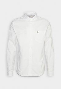 Vit långärmad skjorta i bomullstyg, med klassisk krage, en bröstficka och liten broderad logotyp på fickan.