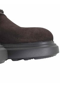 Bruine suède enkellaars met een afgeronde neus, voorzien van een dikke zwarte rubberen zool en een gestructureerd dessin aan de onderkant voor grip.