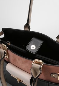 Black and beige handbag with gold hardware, featuring a zippered pocket, magnetic snap closure, and a mix of smooth and suede textures.