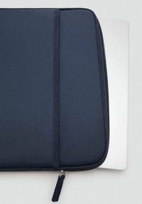 Marineblå laptop sleeve med en glat tekstureret overflade, lynlåslukning og en kvastdetalje; rummer en sølvfarvet laptop, der er synlig nedenunder.