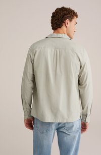 Svetlo zelena, dolg rokav, s sproščenim krojem, gumbnimi manšetami in zadnjim pregibom. V kombinaciji z blede modre kavbojke.