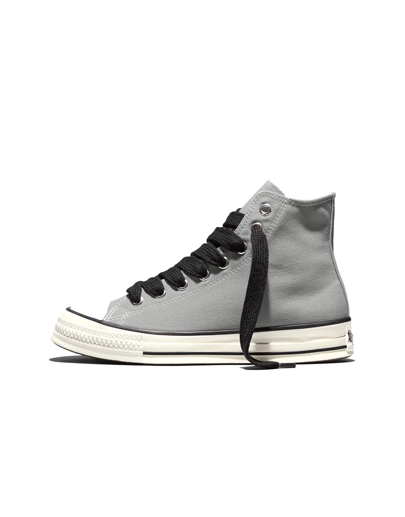 Sneaker grigia alta in tela con lacci neri, suola in gomma bianca e dettaglio a striscia nera, mostrata dal lato esterno su sfondo bianco.