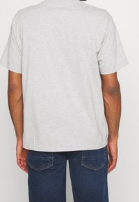 Šedé bavlněné tričko s krátkým rukávem a kulatým výstřihem, má volný střih a jemné švy na ramenou a zádech.