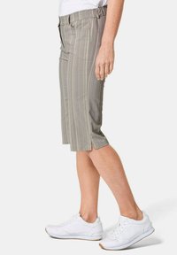 Grijze gestreepte bermuda shorts met een aansluitende tailleband, twee zijzakken en zijsplitten. Gecombineerd met witte sportschoenen.