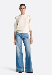 Pulover crem cu mâneci bufante, asortat cu blugi denim largi, de culoare albastru deschis. Ținuta are un design simplu și o textură moale.