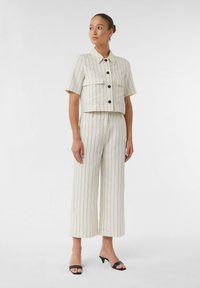 Cropped, white striped blouse with black buttons paired with matching wide-leg trousers. Smooth fabric, short sleeves, and sleek black mules.