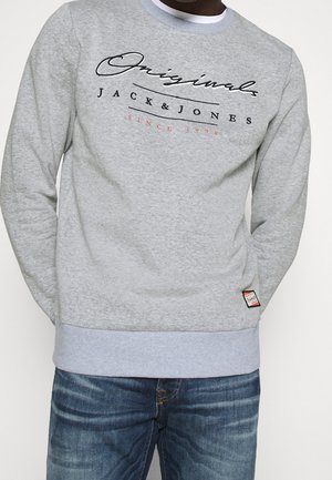 Sweatshirt gris avec un logo en texte noir et rouge "JACK & JONES" sur la poitrine. Poignets et ourlet côtelés, avec une petite étiquette de marque sur le côté.