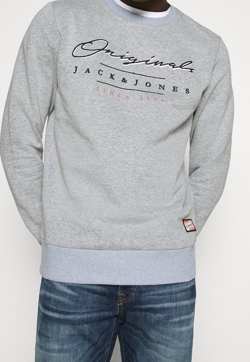 Felpa grigia con logo in testo nero e rosso "JACK & JONES" sul petto. Maniche e orlo a coste, con un piccolo etichetta del marchio sul lato.