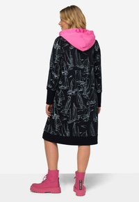 Schwarzes Kapuzenkleid mit weißem Segelboot-Druck, rosa Kapuze, gerippten Bündchen und Saum. Tragen mit rosa Schnürstiefeln in Chunky-Optik.