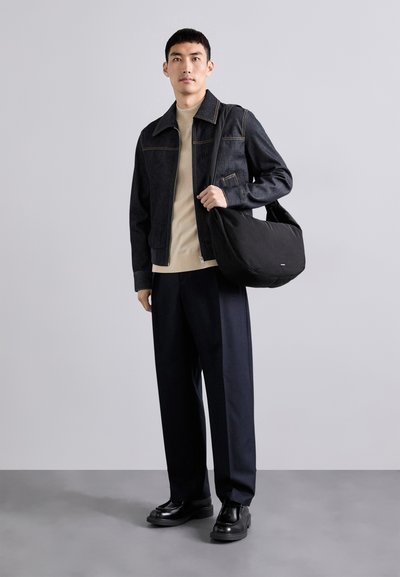 Giacca di jeans scura con cuciture gialle, maglione beige, borsa nera, pantaloni blu navy larghi e scarpe nere con una texture liscia.