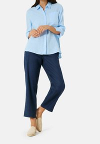 Světle modrá lněná košile s jednou náprsní kapsou, spojená s námořnickými lněnými kalhotami. Model má na sobě béžové nazouvací boty.