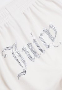 Λευκό ύφασμα με  gathered ελαστική μέση που διαθέτει ασημένια ριχτά διακοσμητικά που σχηματίζουν τη λέξη "Juice" σε καλλιγραφική γραφή.