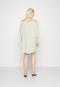 Vestido verde claro, sem alças, com mangas bufantes de três quartos, tecido texturizado e decote com babados, caindo acima do joelho.