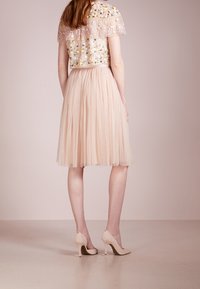 Top corto in pizzo con ricami floreali in tonalità pastello, abbinato a una gonna plissettata color nude e décolleté beige a punta chiusa.
