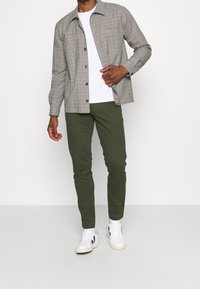 Skjorta med knapp-up i rutigt mönster, tillsammans med olivgröna byxor och vita sneakers. Tyget verkar slätt och lätt.