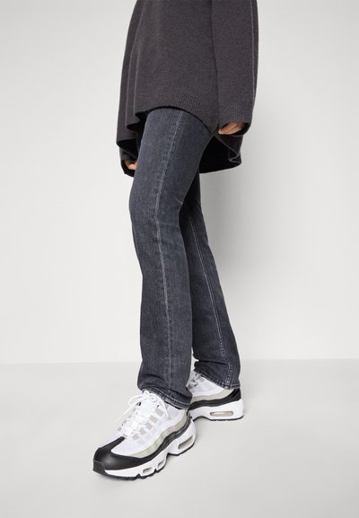 Ciemnoszare dżinsy o slim fit, w zestawieniu z białymi i czarnymi sneakersami z siateczkowej tkaniny oraz charakterystycznym wzorem podeszwy. Przytulny szary sweter.