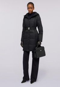 Svart puffjacka med figursydd midja, blixtlås framtill, huva och quiltat mönster. Kallas ihop med svarta handskar och en strukturerad handväska.