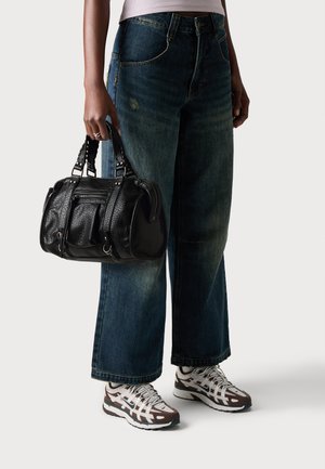Bolso de mano de cuero texturizado negro con doble asa; combinado con unos pantalones de mezclilla de tiro alto, anchos y de un azul deslavado, y zapatillas gris-marrón con detalles blancos.