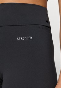 Aukštos juosmens juodos legging'os, pagamintos iš tamprus audinio, su sidabrine siuvinėta užrašu "STRONGER" priekyje. Lygi tekstūra ir prigludusi konstrukcija.