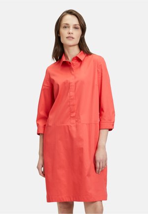 Korallenfarbenes Hemdblusenkleid mit dreiviertelärmligen, Kragen und geradem Schnitt. Aus glattem Stoff mit einem subtilen Glanz gefertigt.