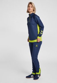 Marinblå och limegrön träningsdräkt med hög krage, långa ärmar med chevrondetaljer och smalnande byxor för en strömlinjeformad passform.