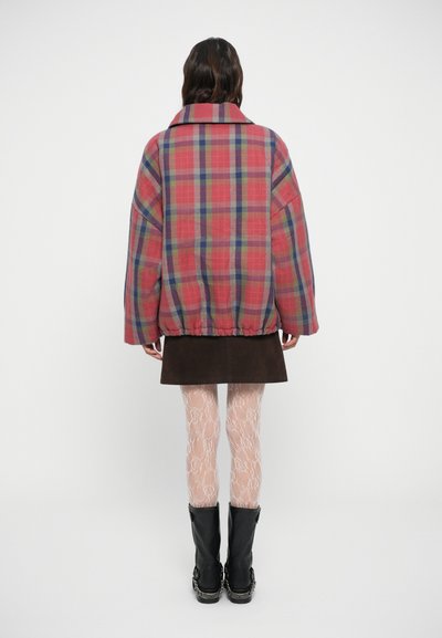 Rød og blå plaid oversized jakke med faldne skuldre, elastisk nederste kant og en bred krave, parret med en brun ruskindsnederdel og mønstrede strømpebukser.