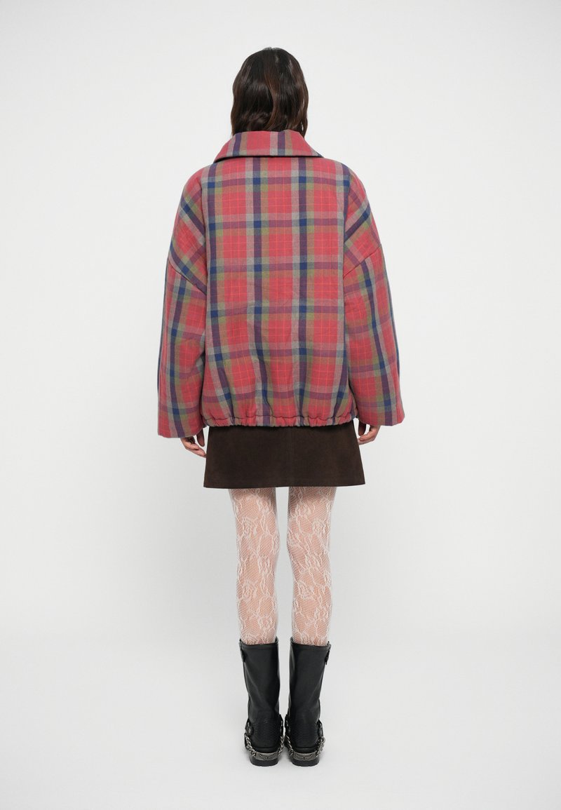 Red and blue plaid oversized jacket with dropped shoulders, elastic hem, and a wide collar, paired with a brown suede skirt and patterned tights.