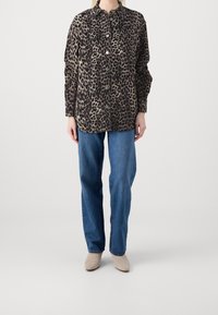 Leopardenmuster-Hemd in Braun und Beige mit Kragen, Brusttasche und leichtem Stoff, kombiniert mit blauen geraden Jeans.