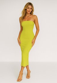 Sukienka midi bez ramiączek w jasnym żółtym prążkowanym materiale, dopasowany krój z rozkloszowanym dołem, zestawiona z jasnobrązowymi sandałami na ramiączkach.