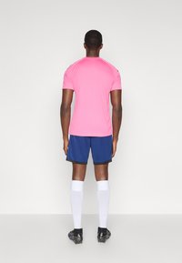 Ρόδινο αθλητικό μπλουζάκι με κοντά μανίκια, μπλε σόρτς, λευκές κάλτσες μέχρι το γόνατο και μαύρα ποδοσφαιρικά παπούτσια, απεικονιζόμενο από πίσω. Απλός σχεδιασμός, αθλητική εφαρμογή.