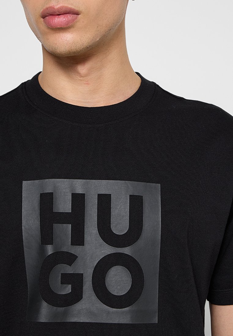 T-shirt en coton noir avec un grand logo carré en lettres noires en relief portant le mot "HUGO", col rond, manches courtes et une coupe régulière.