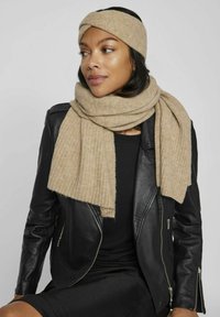 Sciarpa a coste beige con fascia abbinata, realizzata in morbida lana, indossata sopra una giacca di pelle nera, che accentua un look casual.