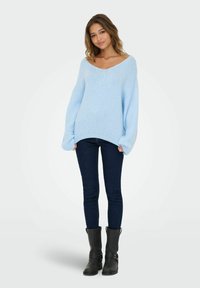 Jasnoniebieski sweter dzianinowy z szerokim dekoltem w kształcie litery V i oversize'owymi rękawami, połączony z ciemnymi dżinsami i czarnymi botkami za kostkę.