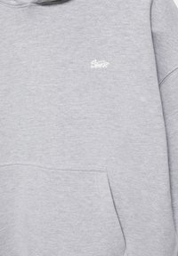 Sweat à capuche gris clair avec une poche kangourou à l'avant et un petit logo blanc brodé sur le côté gauche de la poitrine.