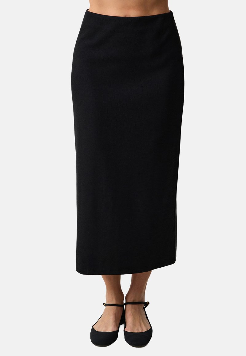Jupe noire mi-longue avec une coupe droite et une texture minimale. Elle présente une taille lisse et est associée à des ballerines noires. Aucune motif visible.