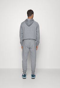 Grau Kapuzenpullover und passende Jogginghose aus weichem Stoff. Mit Kapuze, gerippten Bündchen und schlanker Passform. Die Schuhe sind blau und schwarz.