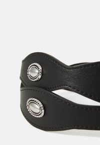 Black leather strap with a smooth texture, featuring silver-tone decorative snaps and contrasting stitching along the edges.