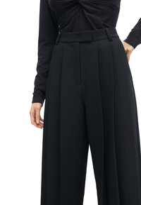 Zwarte plooibroek met een hoge taille, gemaakt van een soepele stof. Voorzien van riemlussen en een getailleerd ontwerp, geschikt voor formele kleding.
