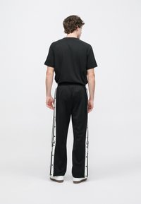 Čierne tričko s krátkym rukávom v kombinácii s čiernymi teplákmi so siedmimi bielymi bočnými gombíkmi a pruhmi, navrhnuté s voľným strihom.