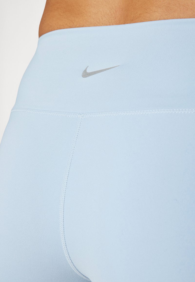 Leggings deportivos de un azul claro, hechos de una tela elástica, con una textura suave y un pequeño logo plateado de Nike en la cinturilla.